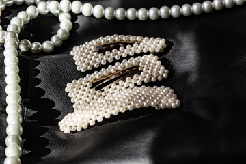 Fototapeta premium Beautiful and fashionable decoration of white beads of pearls, a nice milky color, on a black leather background. Hair accessories, round and large.
