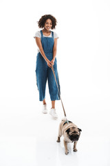 Image of attractive african american woman holding leash and walking with her pug dog