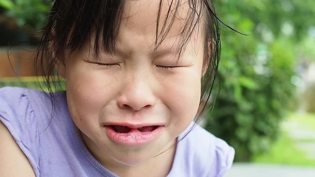 Unhappy little asian girl sitting in park and crying alone,slow motion.