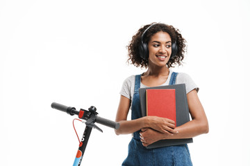 Image of smiling african american woman using headphones and holding exercise books while riding on...