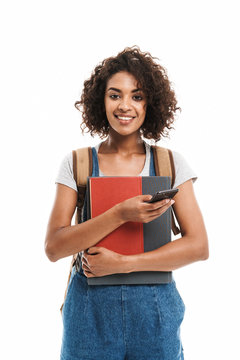 Image of pretty african american woman wearing backpack holding exercise books and cellphone