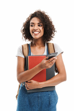 Image of beautiful african american woman wearing backpack holding exercise books and cellphone