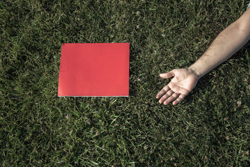 hand and red book on grass
