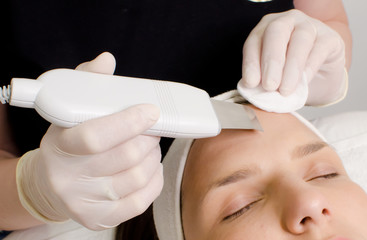 Cosmetologist,beautician in white gloves  making facial treatment with ultrasonic spatula to young woman,face skin scrubber treatment with ultrasonic spatula,facial cleansing procedure in beauty salon