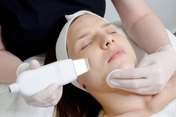Cosmetologist,beautician in white gloves  making facial treatment with ultrasonic spatula to young woman,face skin scrubber treatment with ultrasonic spatula,facial cleansing procedure in beauty salon
