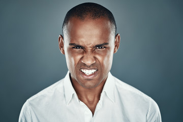 Fototapeta premium Getting angry. Displeased young African man in shirt looking at camera and frowning while standing against grey background