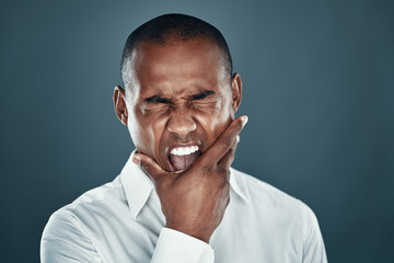 Making a face. Displeased young African man in shirt keeping eyes closed and shouting while standing against grey background