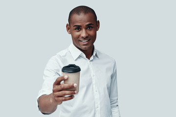 Want some? Handsome young African man giving you disposable cup while standing against grey background