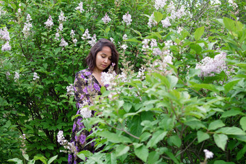 Portrait of beautiful young woman in black-purple dress in a garden with blooming lilac bushes.
