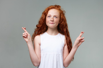Portrait of wishful nice little girl with ginger hair and freckles, calming smiles and looks up,...