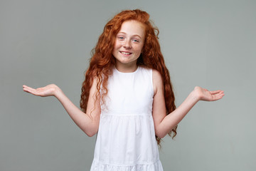 Portrait of distracted nice little girl with ginger hair and freckles, looks confused, spreads his...