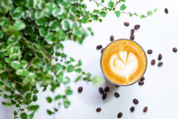 a glass of hot latte coffee on white coffee table with green plant