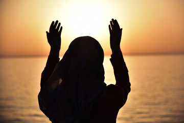 Silhouette of a muslim women praying during sunset on the big ship. Back view of muslim woman praying wearing hijab.