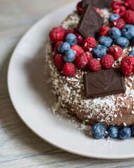 Homemade chocolate berry cake with coconut chips lies on wooden grey background, natural light, copy space 