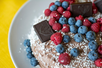 Homemade chocolate berry cake with coconut chips lies on wooden grey background, natural light, copy space 