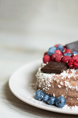 Homemade chocolate berry cake with coconut chips lies on wooden grey background, natural light, copy space 