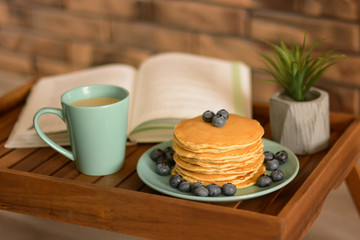 Pancakes with blueberries, cap of coffee and book on the bed table