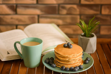 Pancakes with blueberries, cap of coffee and book on the bed table