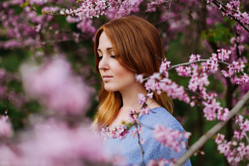 Beautiful smilling redhead woman in spring time blossom cherrytrees garden.