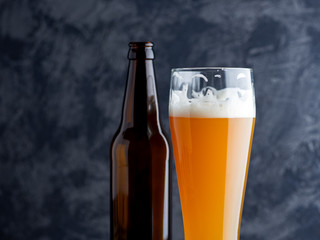 Close-up of a glass of cold unfiltered wheat beer and a beer bottle on a dark background