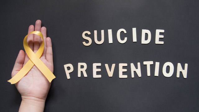 World suicide prevention day - Human hands holding yellow ribbon awareness symbol for preventing suicide on black background. Mental health care concept.