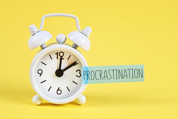 Procrastination, delay, urgency concept. White alarm clock with text procrastination.