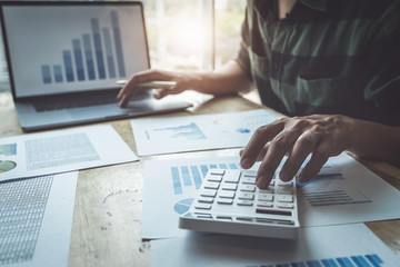 Business man using calculator to review balance sheet annual with holding pen and using laptop...