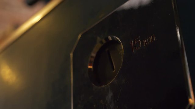 Someone's hand is carefully inserting small coin into coin-slot with metallic square frame which has shining mirror-like surface.