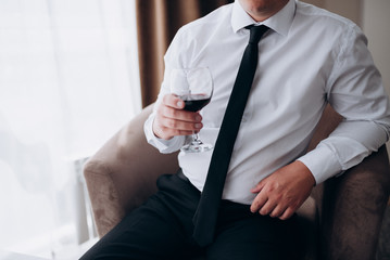 a man in a white shirt with a black tie and black trousers holding a glass of red wine