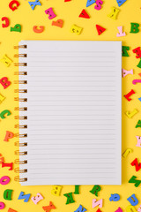 Open empty notebook and colorful letters on a yellow background. Top view. Space for text or design.