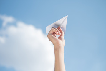Men's hands holding a white paper rocket with a bright blue background.