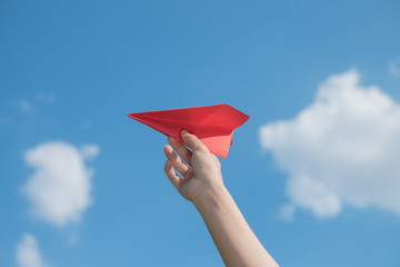 Woman hand holding a red paper rocket with a bright blue background.