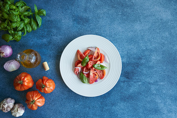 Vegetable tomato salad with extra virgin olive oil, purple onion, purple garlic and basil. Accompanied by a bottle of extra virgin olive oil, purple onions, purple garlic and a bouquet of basil.