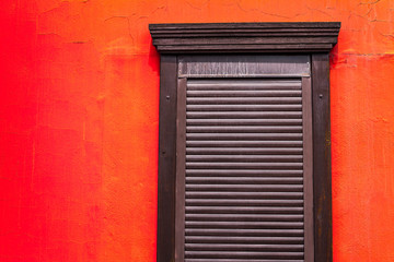 brown shutters on a wooden window on a wall painted in bright red-orange color