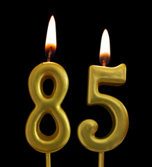 Burning golden birthday candles on black background, number 85