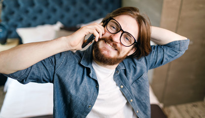 Bearded man wearing glasses speaking on the smartphone at the bedroom