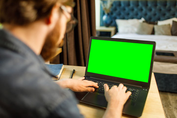 Bearded man working at the home for a laptop with a green screen