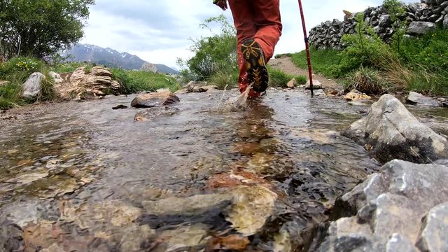 hiker woman crossing a small stream in the mountain