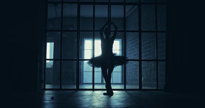 Ballerina rehearsing dance in a dark hall. Silhouette dancer.