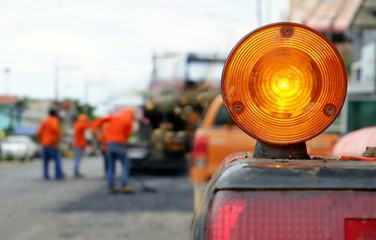 Focus on yellow warning sign of road roller parking on roadside with blurred background of workers group and asphalt paver are working on the street