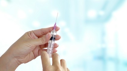 Close up female doctor hand holding syringe with blurred medical office background, medical health care concept