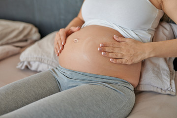 Young pregnant woman rubbing moisturising cream on her belly to moisturise her skin and reduce the possibility of stretch marks after childbirth - obrazy, fototapety, plakaty