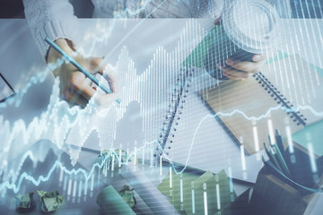 Fototapeta premium Financial forex graph displayed on hands taking notes background. Concept of research. Multi exposure