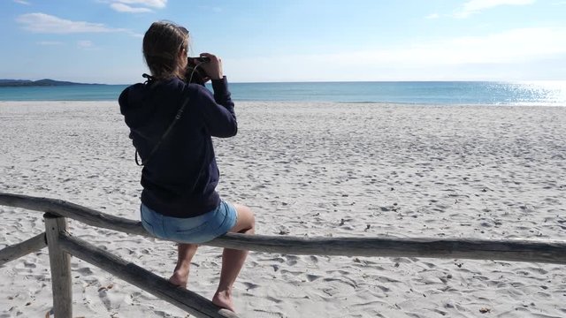 SLOW MOTION Unrecognizable young woman sitting on a wooden fence taking pictures