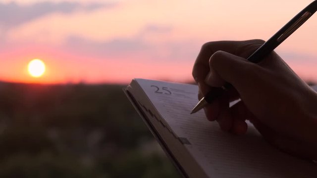 Businessman writing ideas in a notebook at sunset. Men makes notes in a notebook on paper at sunset. Concept of generating ideas and business projects