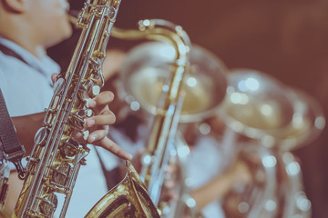 Male student with friends blow the saxophone with the band for performance on stage at night.