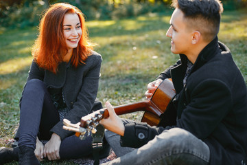 Fototapeta premium Cute couple in a park. Lady with red hair. Guy with a guitar