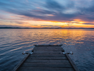 Naklejka na ściany i meble Calm and meditation concept. Sunset on the lake, wooden bridge in the foreground, quiet water, cloudless sky. Blue hour