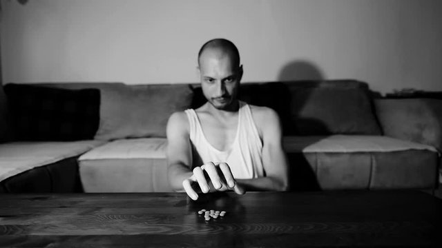 Depressed man suffering from suicidal depression want to commit suicide by overdose taking strong medicament drugs and pills pain killers sitting in his dark room selective focus moody dramatic look