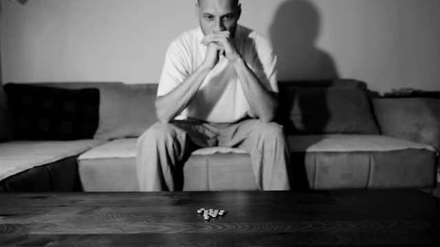 Depressed man suffering from suicidal depression want to commit suicide by overdose taking strong medicament drugs and pills pain killers sitting in his dark room selective focus moody dramatic look